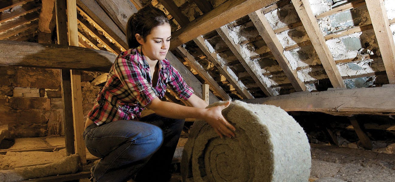 Woman unrolling and laying loft insulation